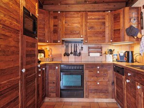 Eine rustikale Küche mit Holzschränken, einem eingebauten Ofen und verschiedenen Küchenutensilien, die an der Wand hängen.