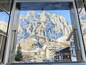 Une vue sur une montagne, aperçue à travers une fenêtre à cadre en bois, avec une ville en contrebas, des bâtiments et une route.