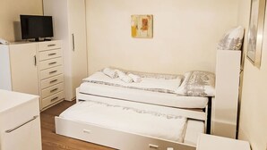 Una habitación pequeña y acogedora con una cama, un televisor sobre un mueble y un cuadro en la pared.