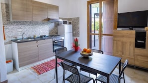 Une cuisine compacte équipée d’une cuisinière à gaz, d’un four à micro-ondes et d’un réfrigérateur, ainsi que d’une table à manger avec des chaises et d’un téléviseur posé sur un meuble en bois.