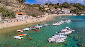 Une zone côtière où des bateaux sont amarrés le long de la rive, avec une plage de sable fin et des bâtiments en arrière-plan.