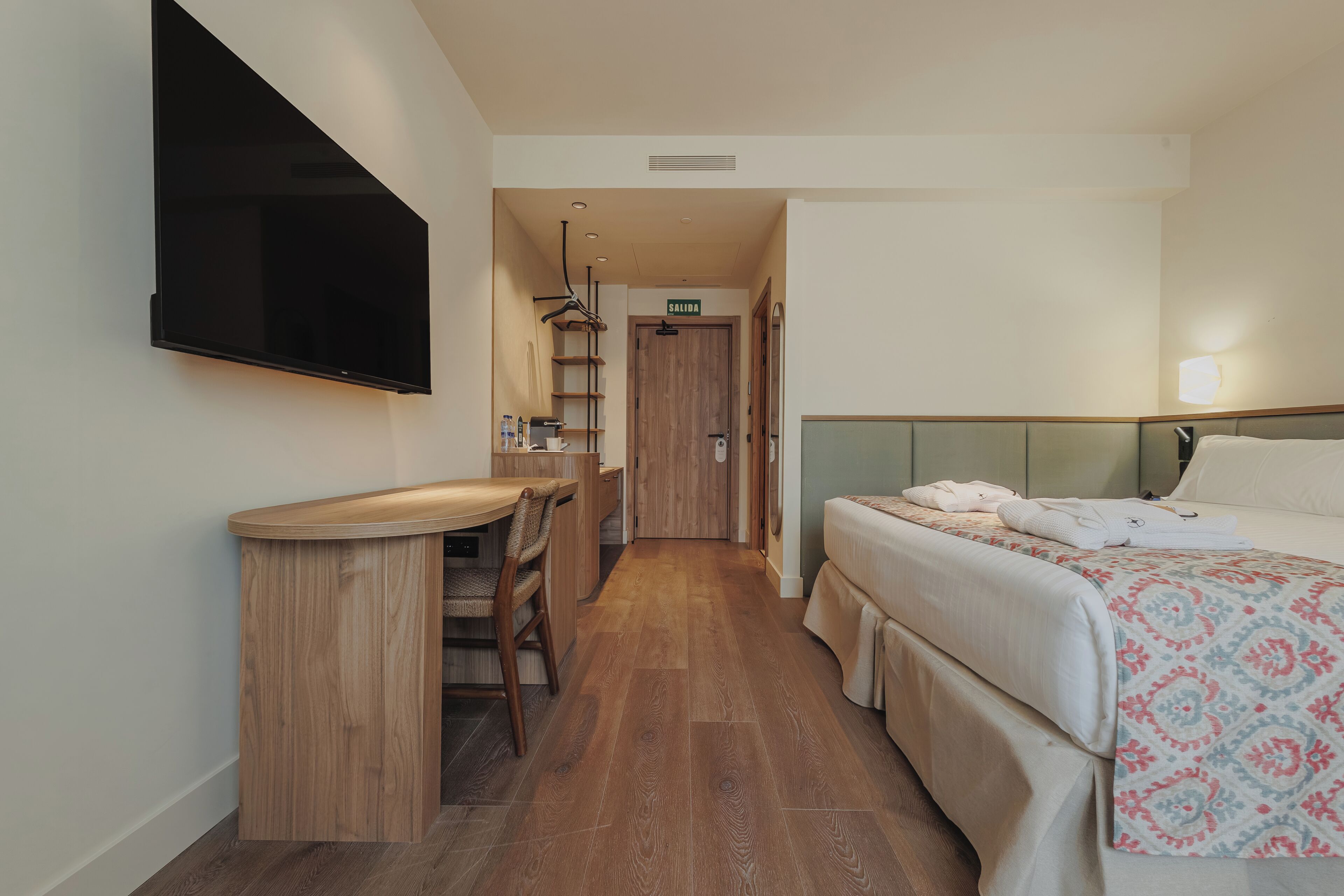 Une chambre d’hôtel avec un lit, un bureau, une chaise, une télévision et une porte de salle de bain.