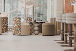 Un interior moderno con un área de estar que incluye sofás, otomanas, una mesa central y vistas amplias a través de grandes ventanales.