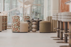 Un interior moderno con un área de estar que incluye sofás, otomanas, una mesa central y vistas amplias a través de grandes ventanales.