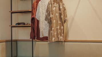 Een hotelkamer met een bed, een houten nachtkastje, een inbouwkast en een kledingroede met kleding.