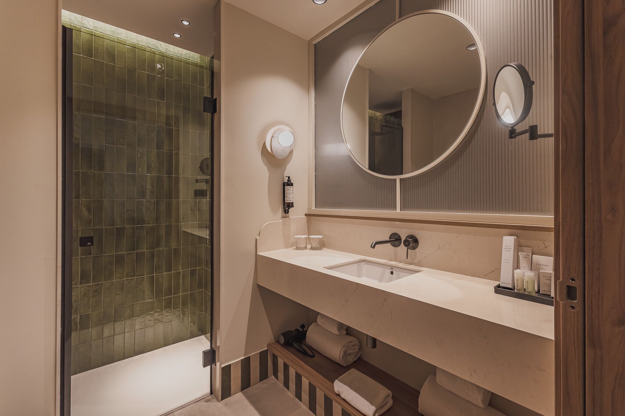 A modern bathroom with a glass shower enclosure, a large mirror, and a vanity with toiletries.