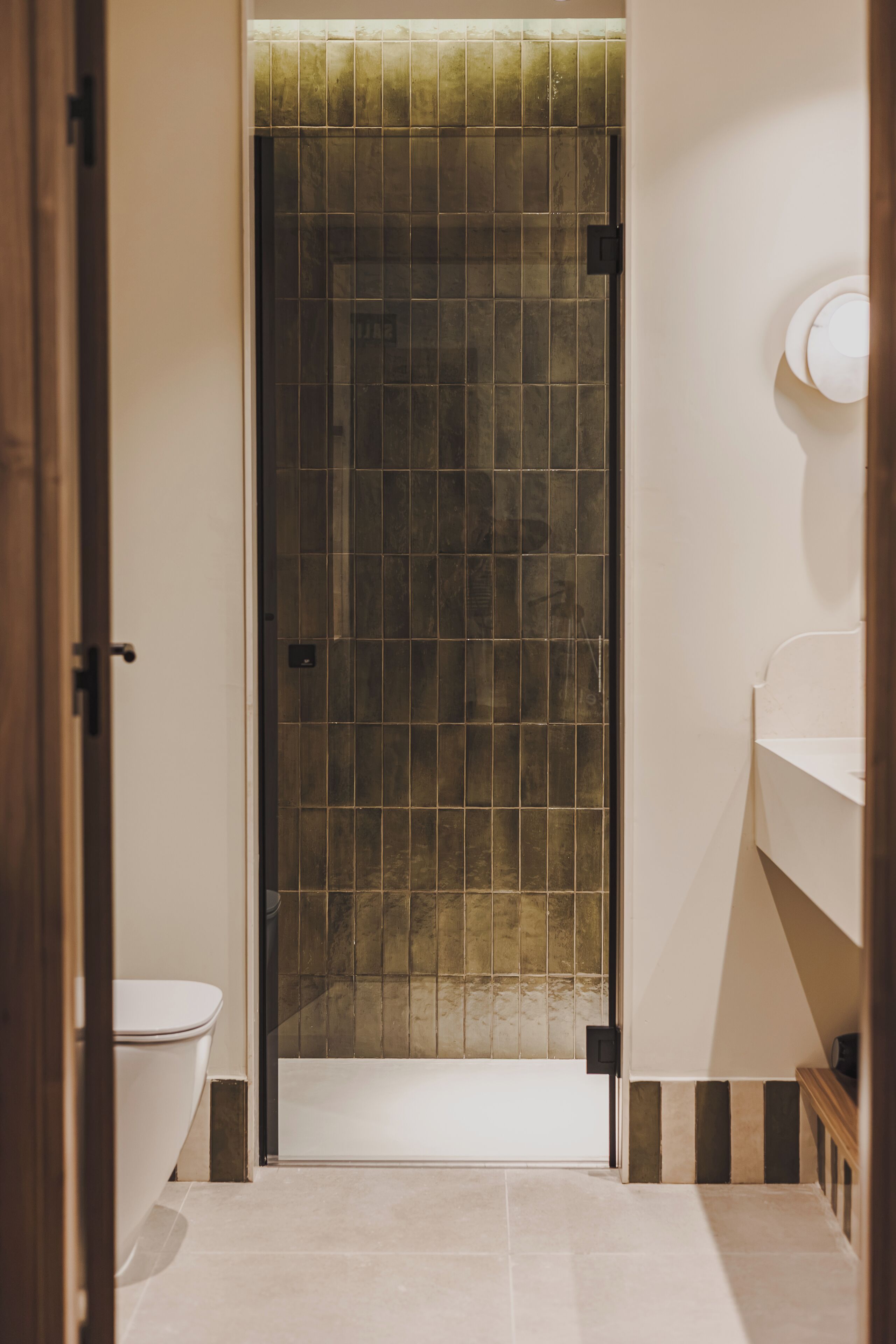 A bathroom with a tiled shower door, a toilet, and a sink.