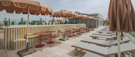An outdoor seating area with tables and chairs, umbrellas, and a view of the cityscape.
