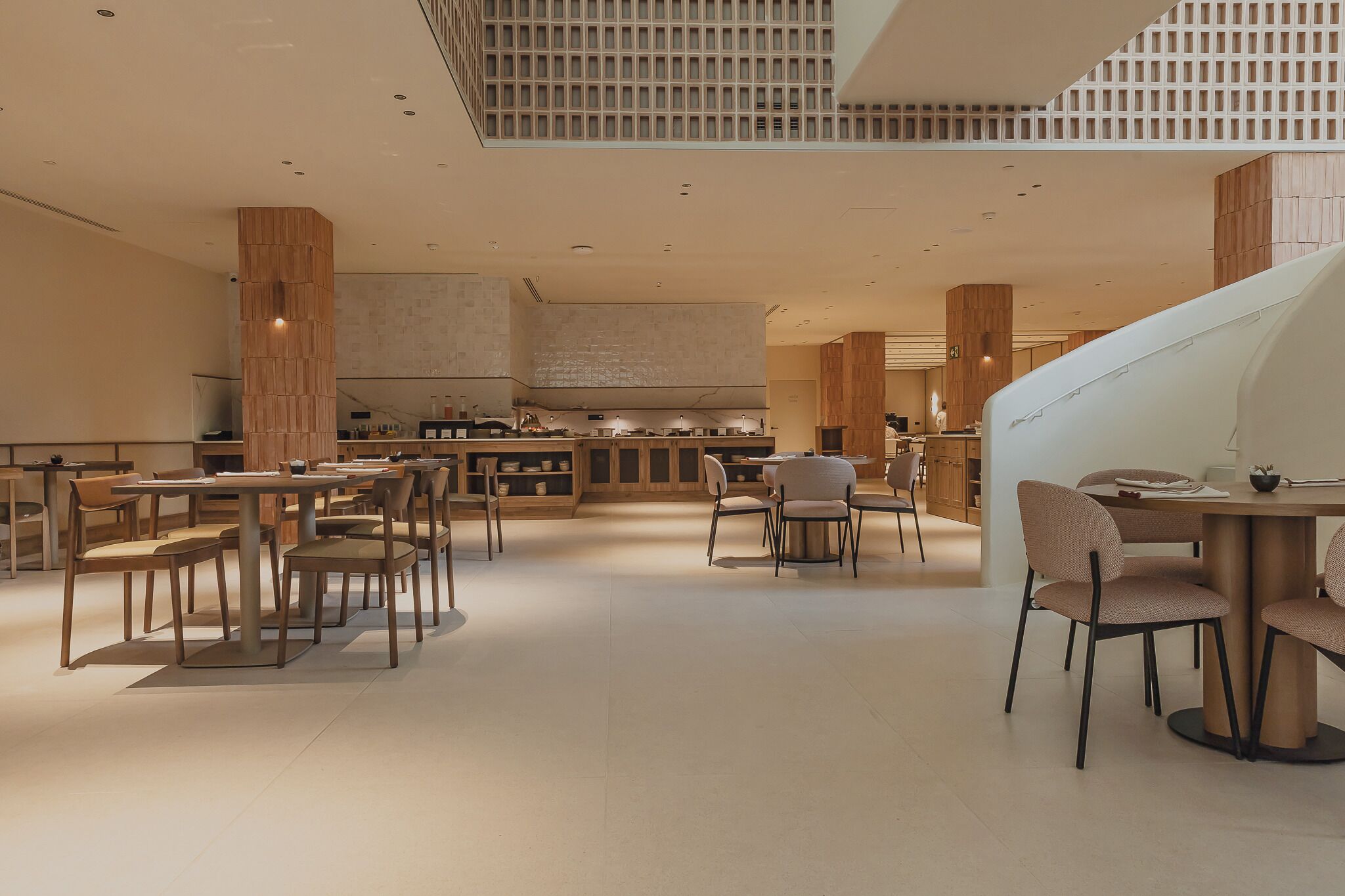 Un amplio vestíbulo de hotel con una zona de bar central, varios espacios de descanso y un alto techo con un diseño de cuadrícula.