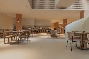 Un amplio vestíbulo de hotel con una zona de bar central, varios espacios de descanso y un alto techo con un diseño de cuadrícula.