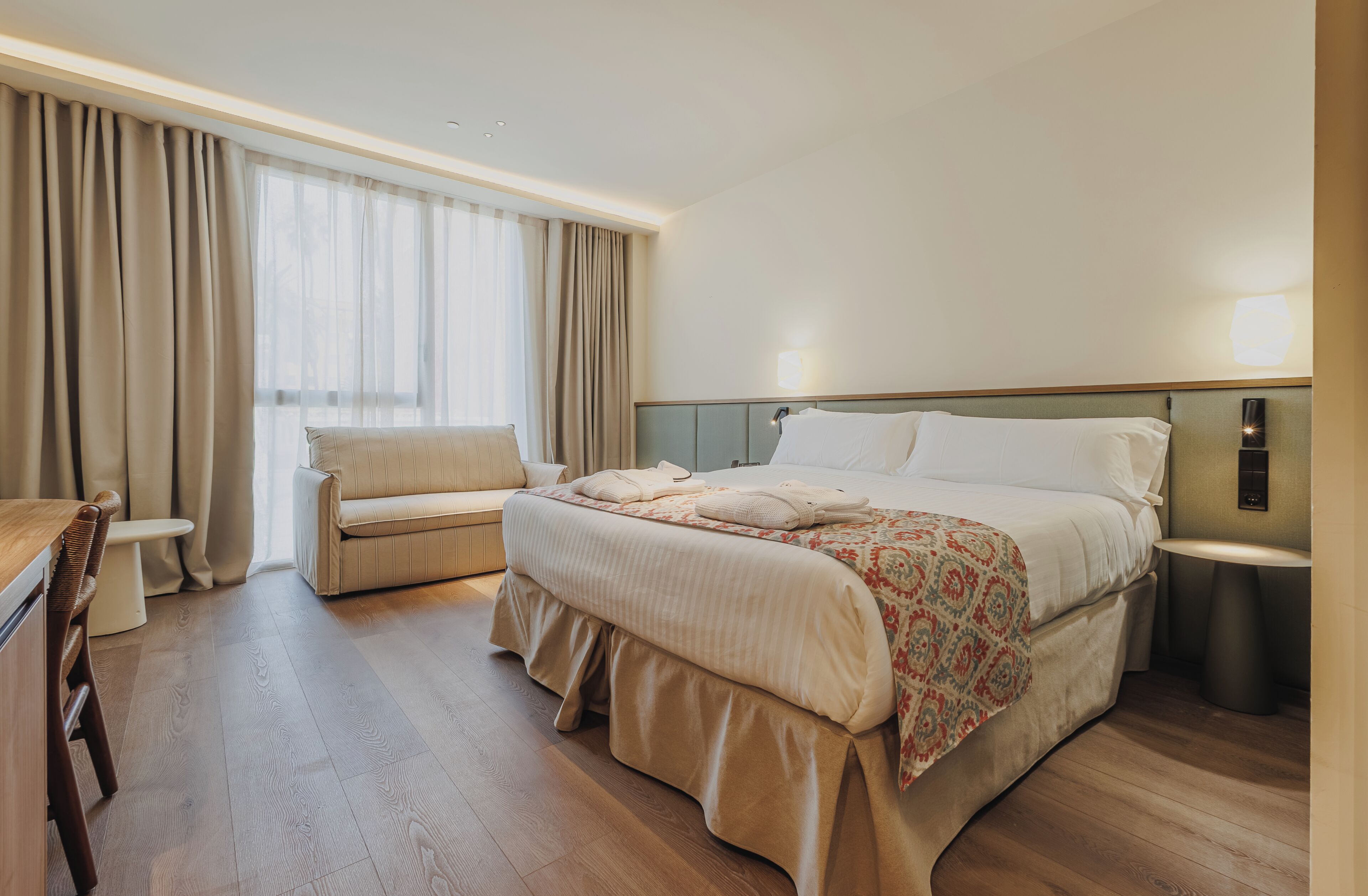 A hotel room with a bed, a sofa, a desk, and a bathroom.
