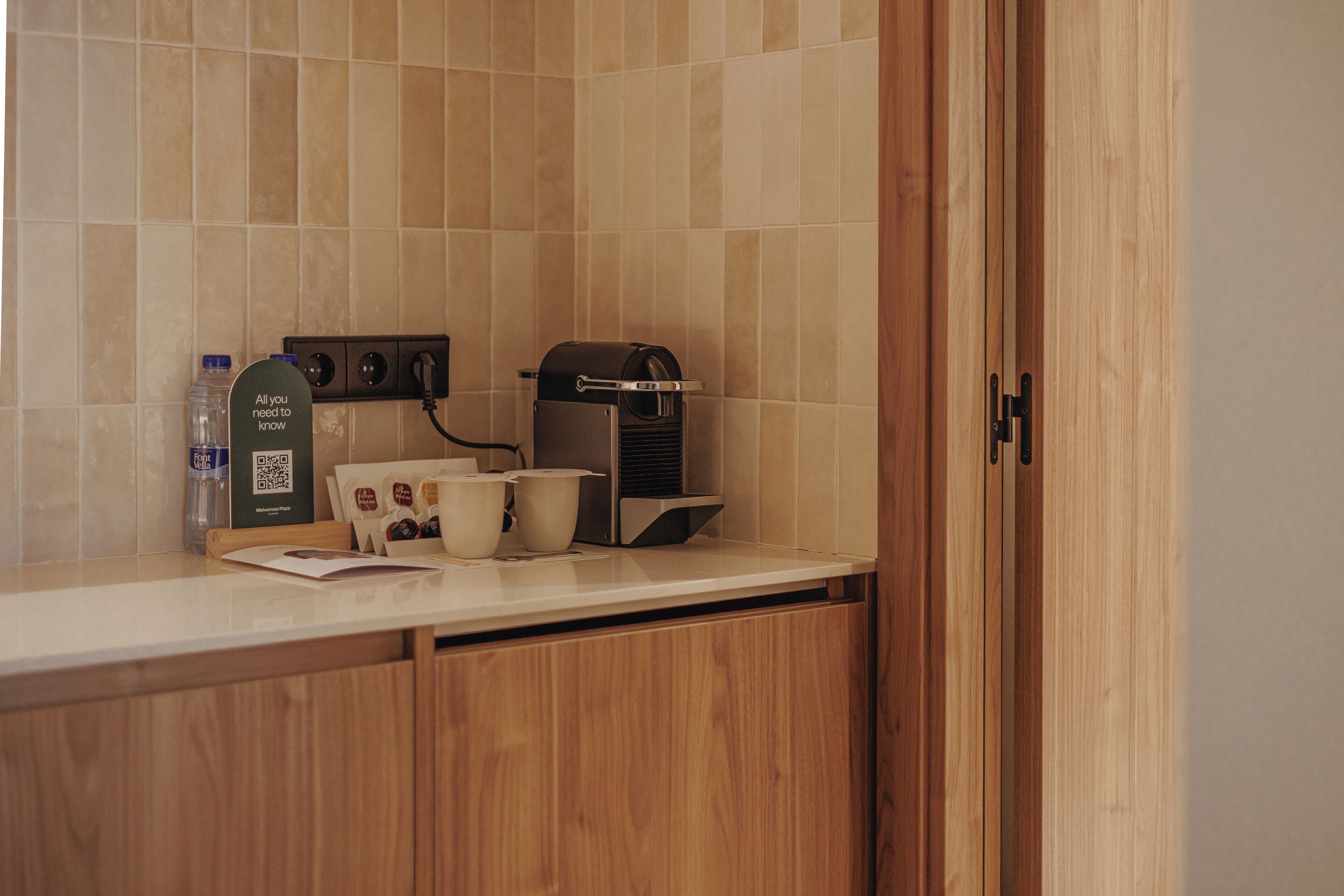A kitchenette with a coffee machine, a water bottle, and a cup on the counter.