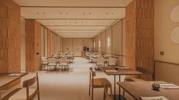 Una amplia sala de conferencias con varias mesas y sillas, paneles de madera en las paredes y una paleta de colores neutros.