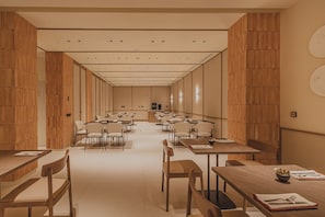 A spacious conference room with multiple tables and chairs, wooden paneling on the walls, and a neutral color palette. - Malvarrosa Plaza by Intelier (Valencia)