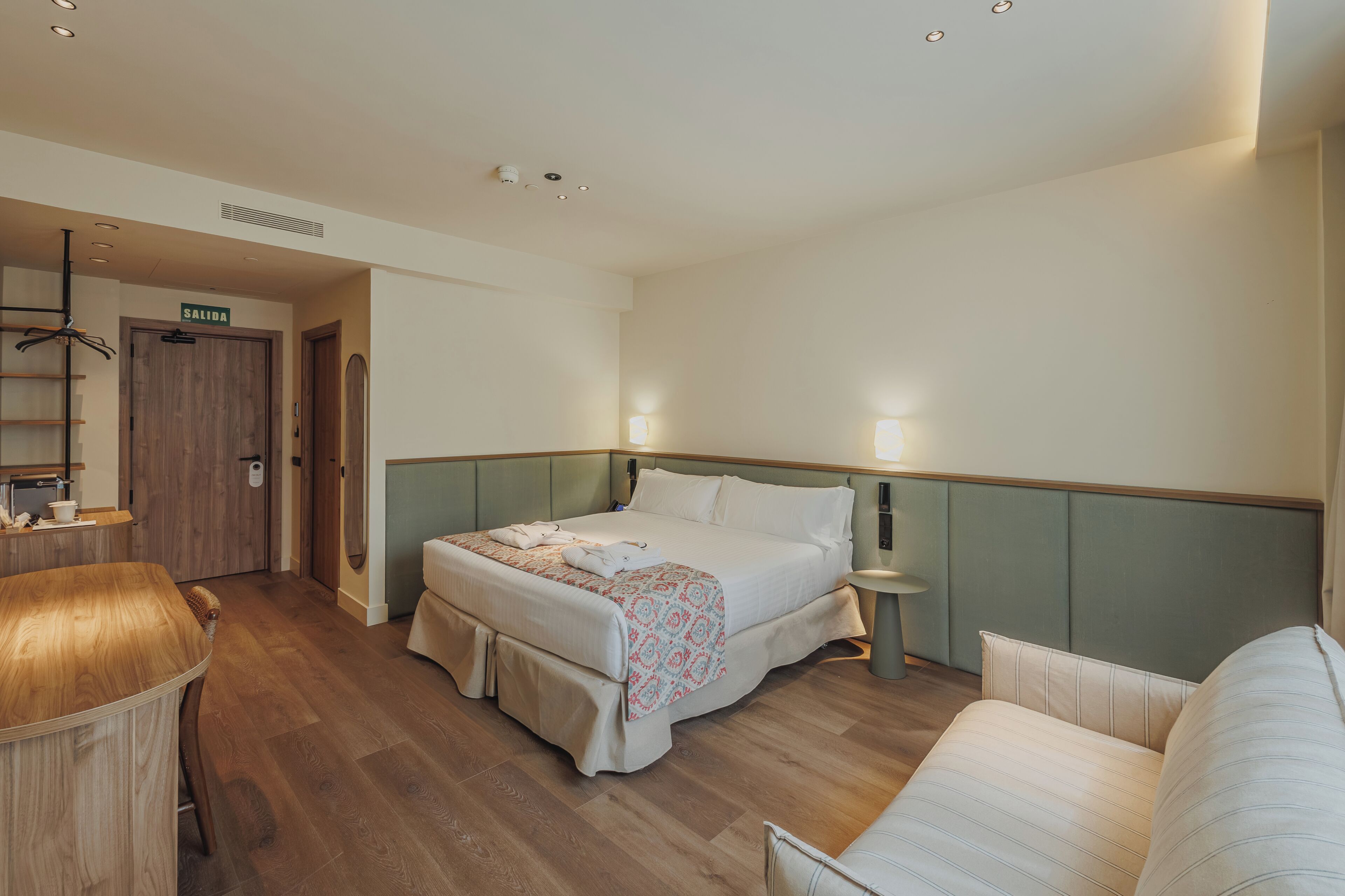 A hotel room with a bed, bedside table, lamp, and a seating area with a sofa.
