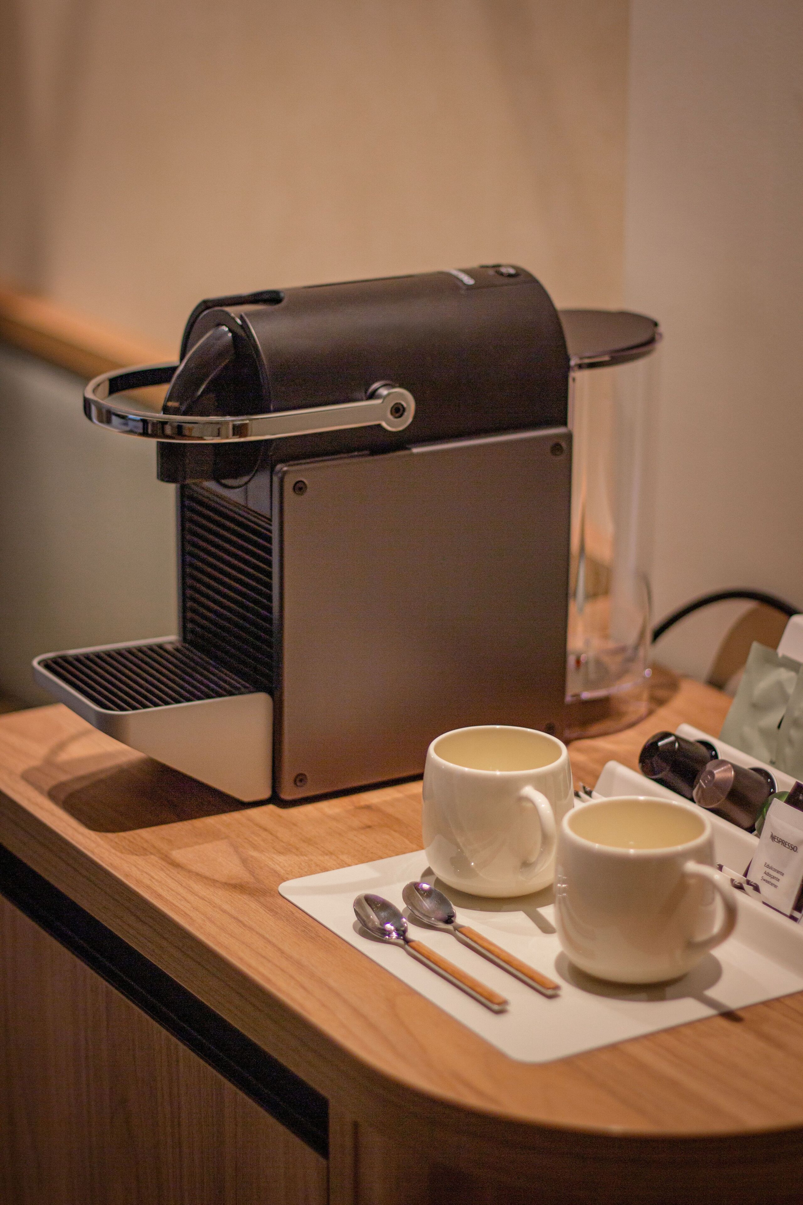 Una máquina de café con dos tazas y una cuchara sobre una encimera de madera.