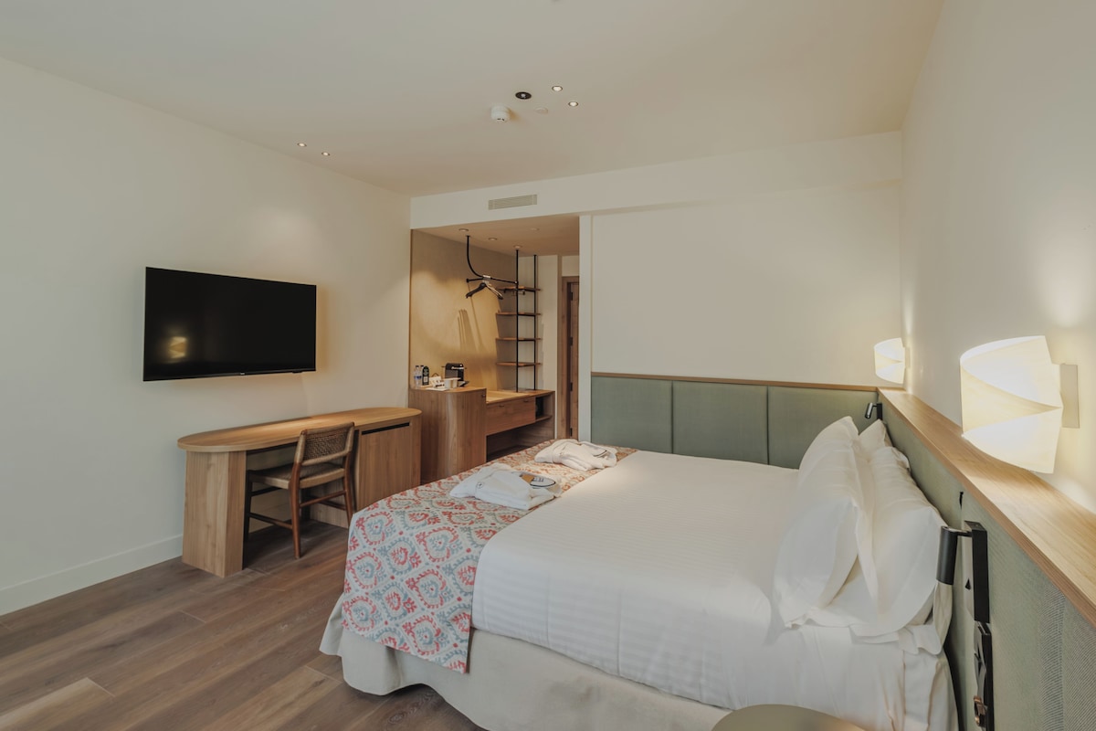 A hotel room with a bed, a desk, a chair, a television, and a wardrobe.