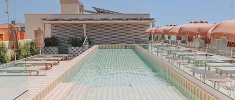 Una piscina en la azotea con suelo a cuadros, rodeada de tumbonas y mesas.