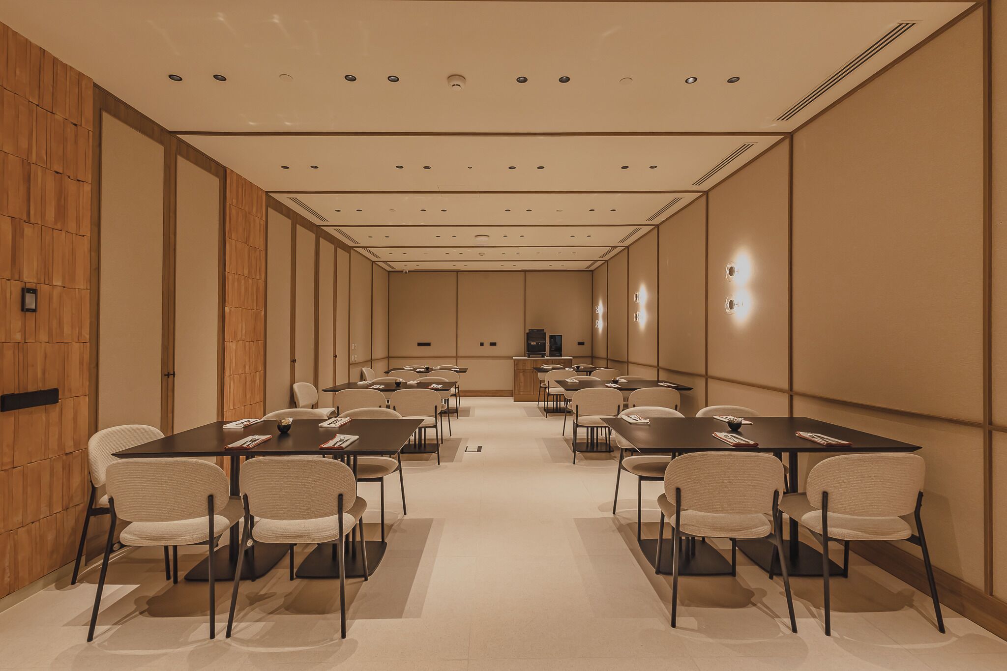 Un salón de conferencias con varias mesas y sillas, paneles de madera en las paredes e iluminación empotrada en el techo.