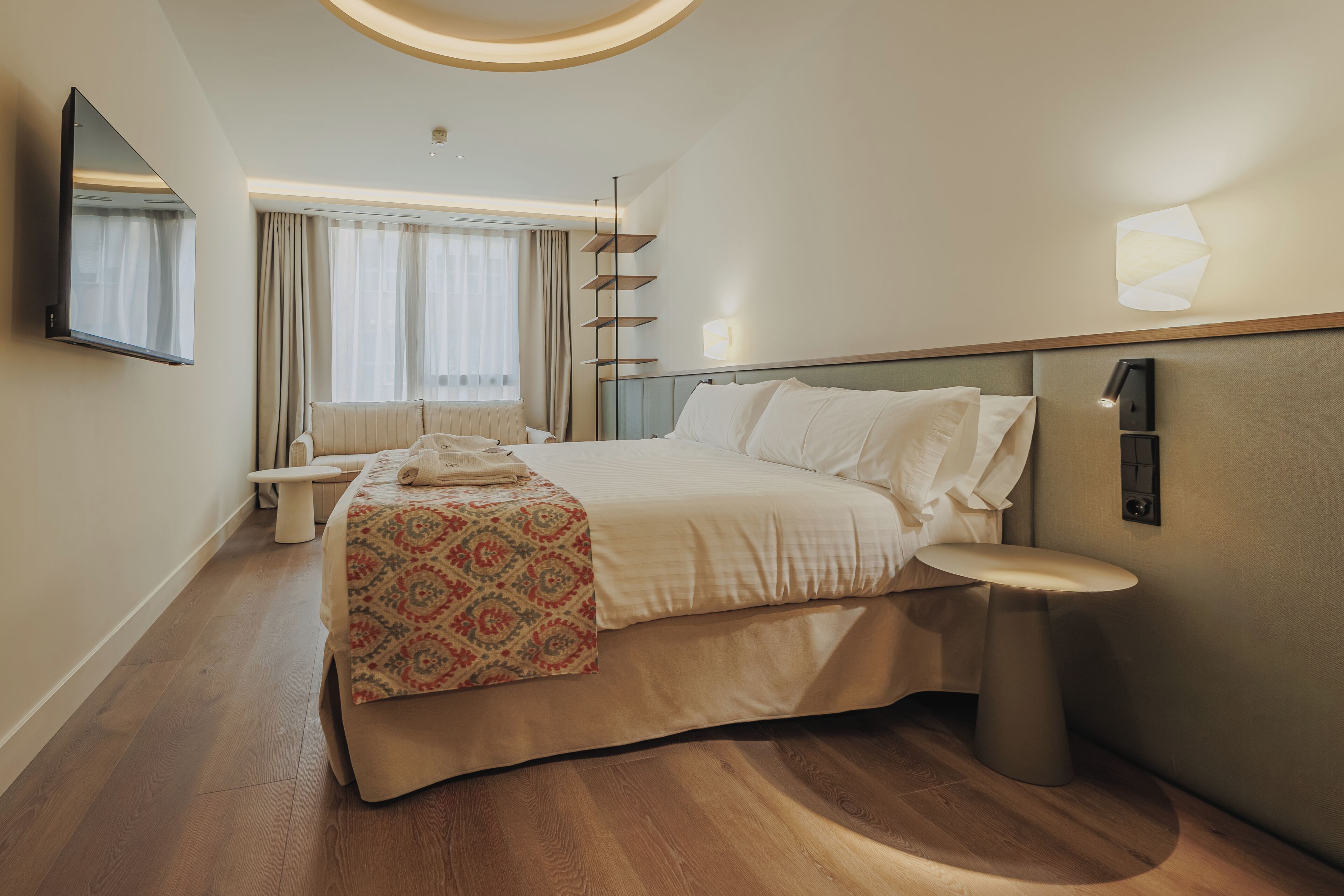 A hotel room with a bed, bedside table, and a large window with curtains.