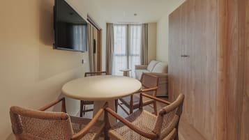 Habitación compacta con una mesa redonda, cuatro sillas de mimbre, un sofá, un televisor montado en la pared y un armario de madera.