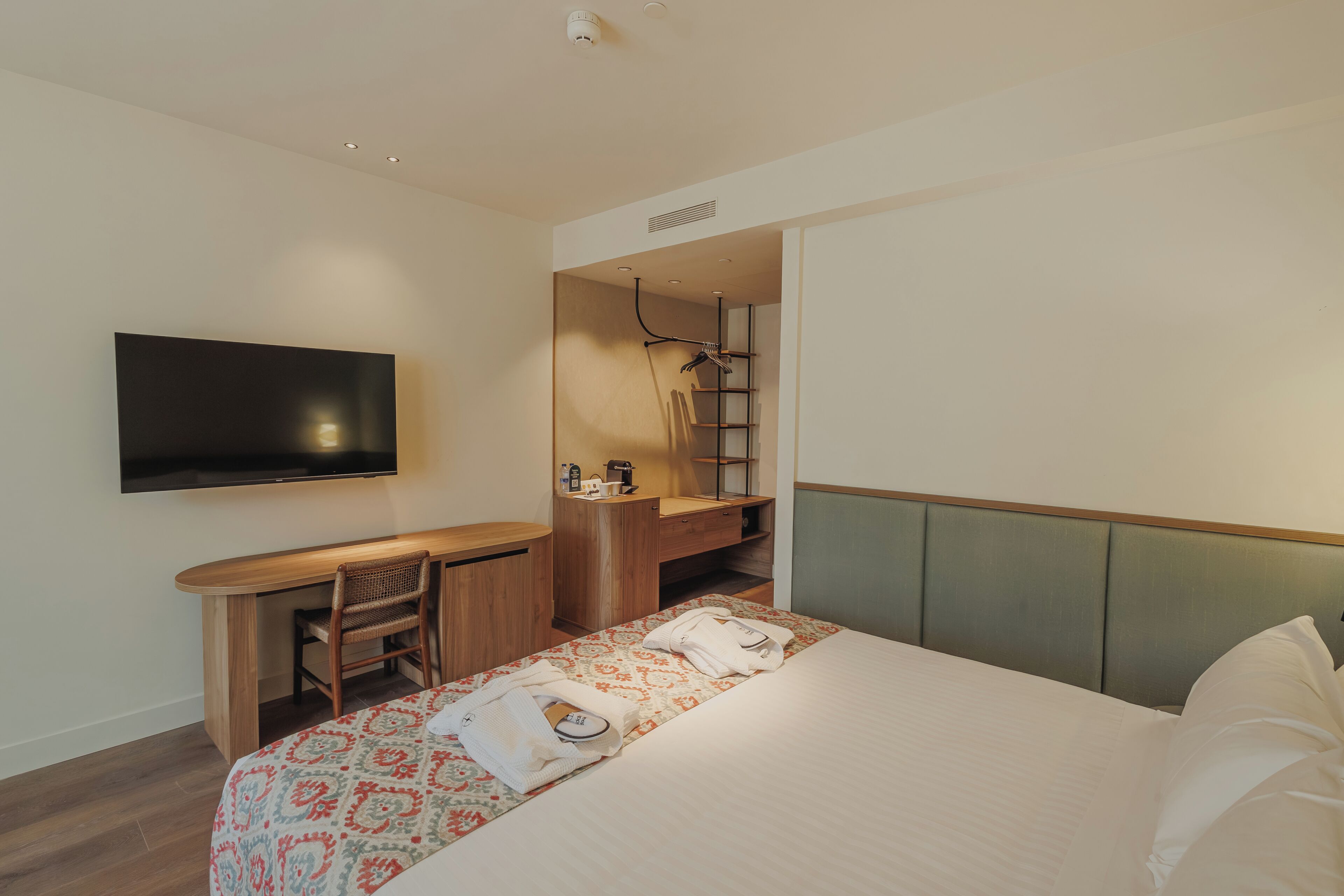 Habitación de hotel con cama, escritorio, silla, televisión y zona de ducha.