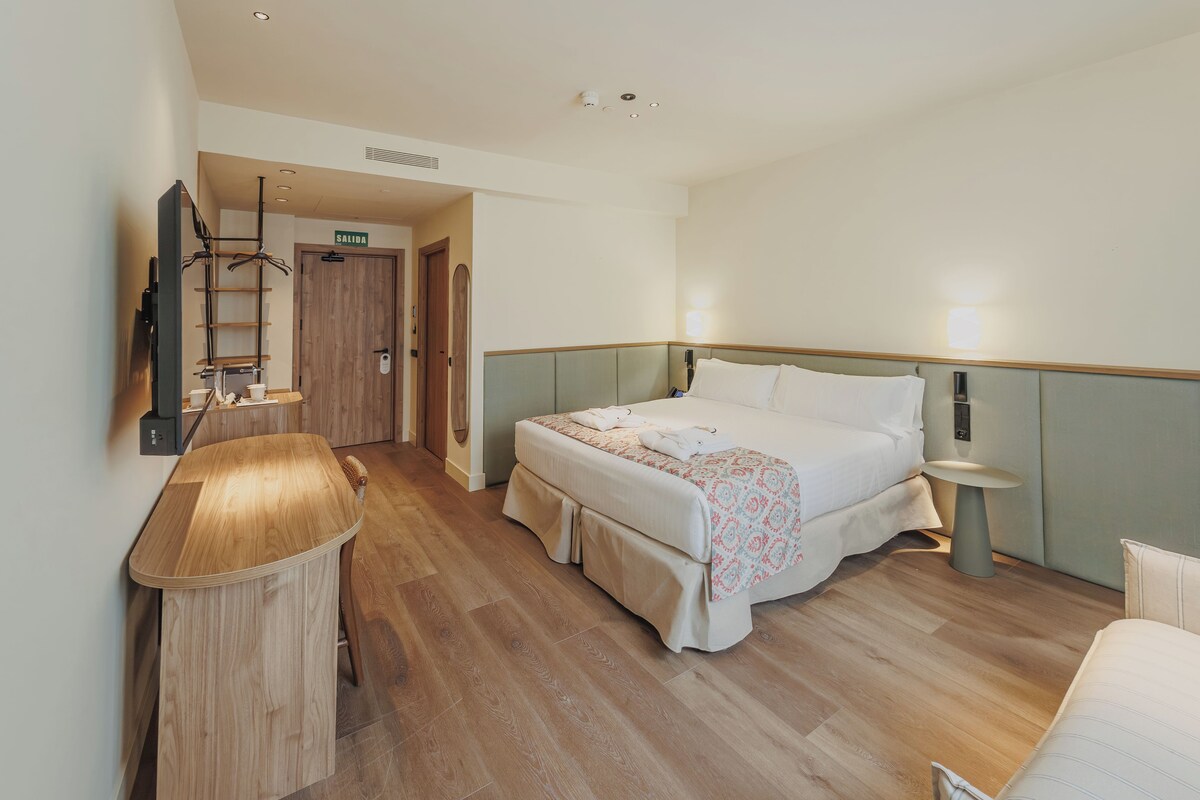 A hotel room with a bed, bedside tables, a desk, a chair, a wardrobe, and a mirror.