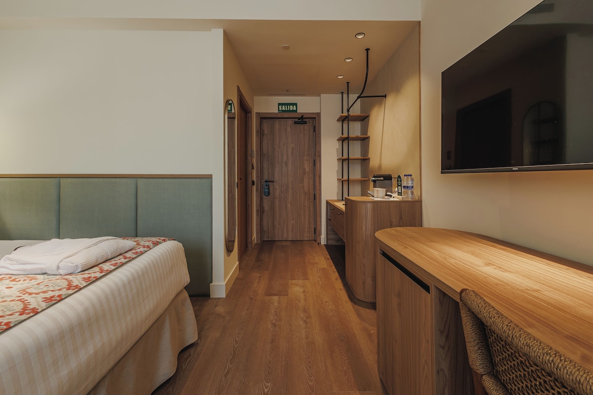 Una habitación de hotel con una cama, un escritorio, un espejo y un televisor.