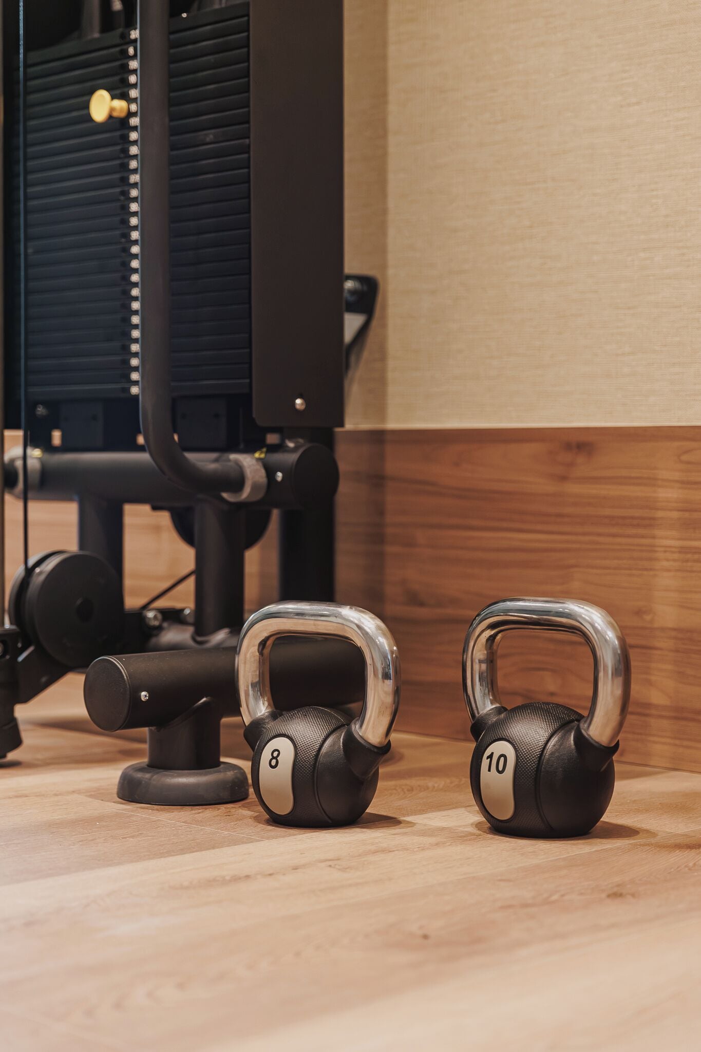Due kettlebell su un pavimento di legno, con attrezzatura ginnica sullo sfondo.