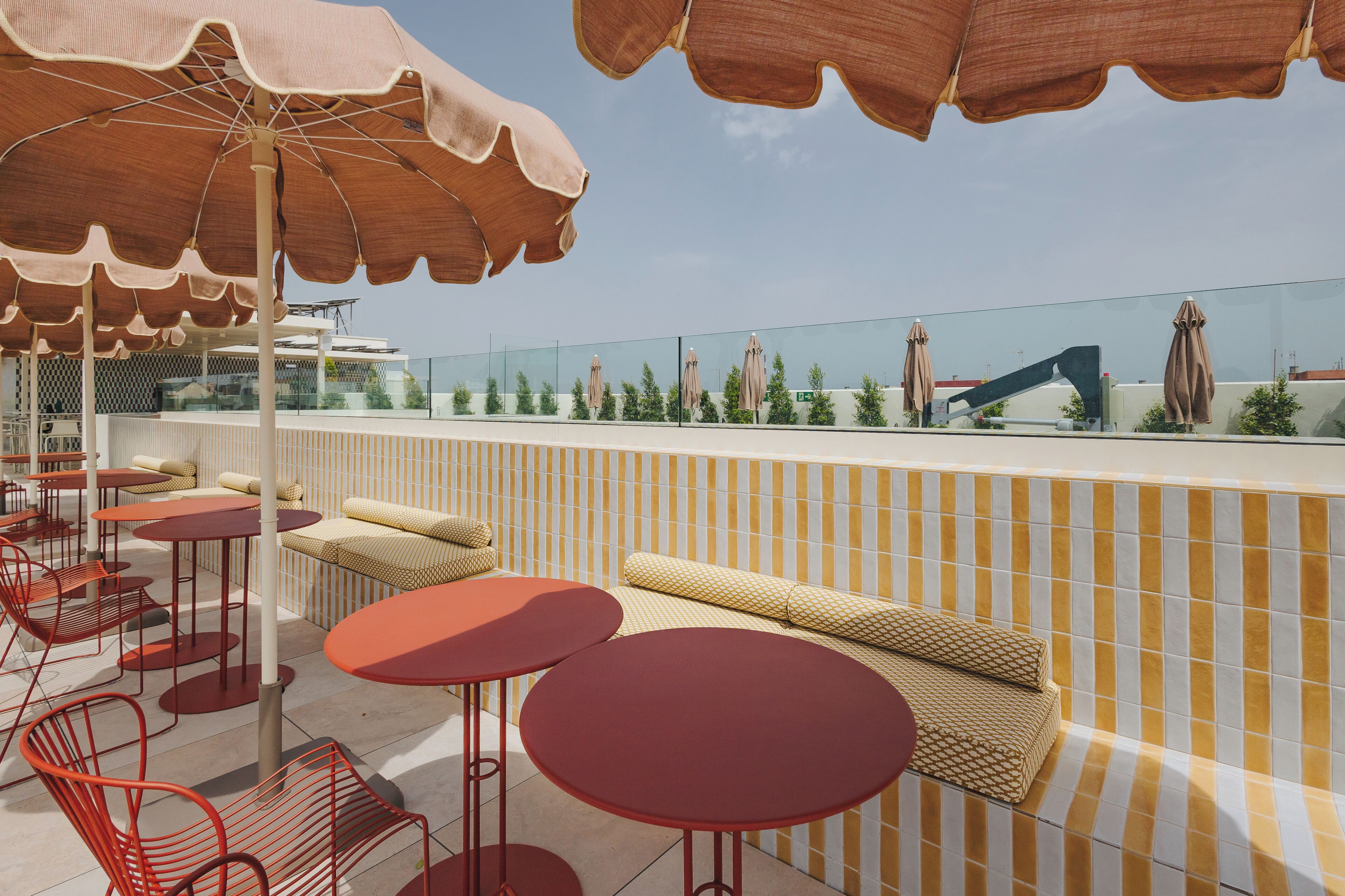 A rooftop terrace with outdoor seating, including round tables and chairs, and umbrellas providing shade.