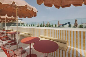 A rooftop terrace with outdoor seating, including round tables and chairs, and umbrellas providing shade. - Malvarrosa Plaza by Intelier (Valencia)