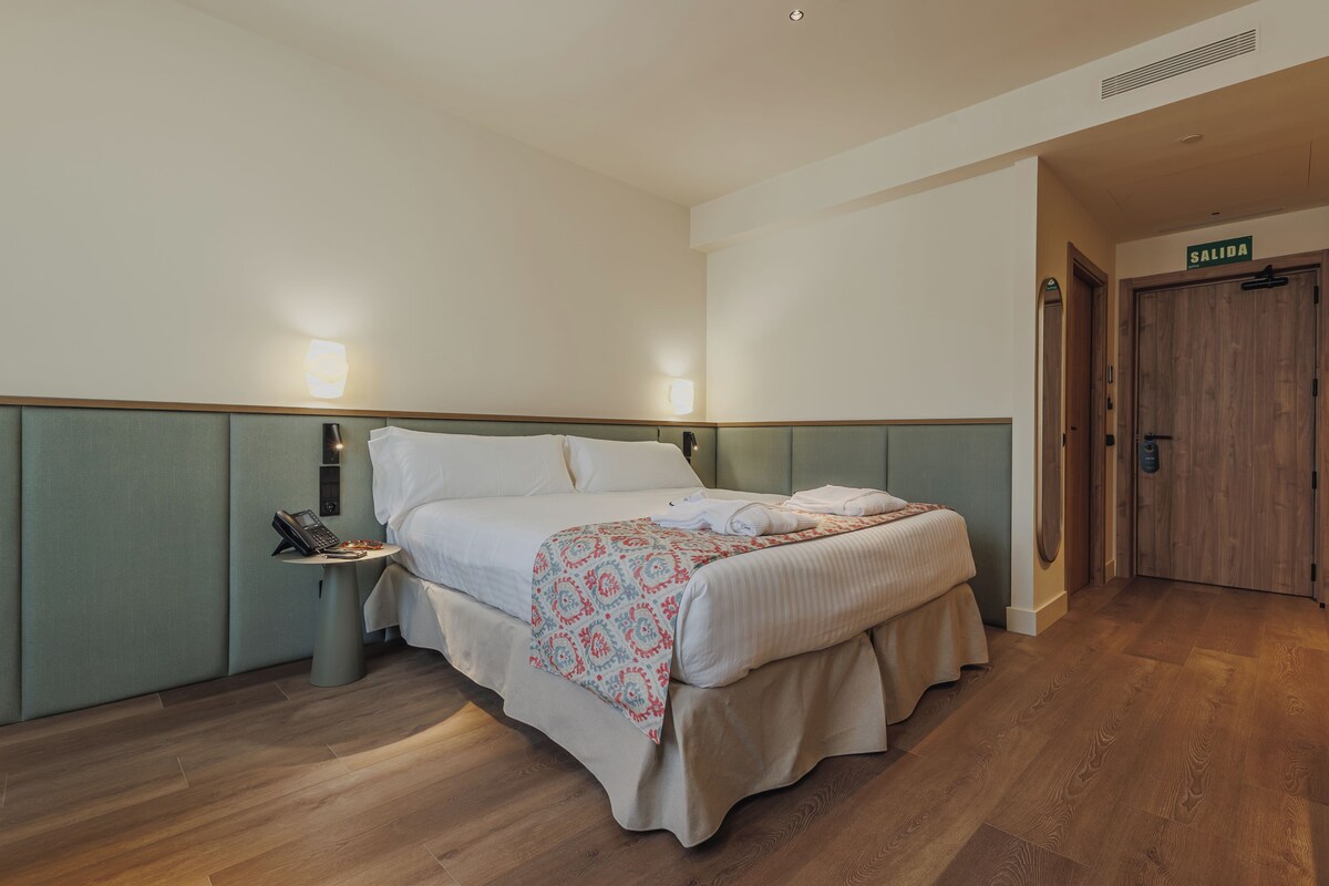 Una camera d'albergo con un letto, un comodino e una porta con la scritta 'SALIDA'.