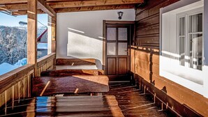 Una escalera de madera que lleva a una puerta con paneles de vidrio esmerilado, con vistas a un paisaje nevado y una ventana con persianas.