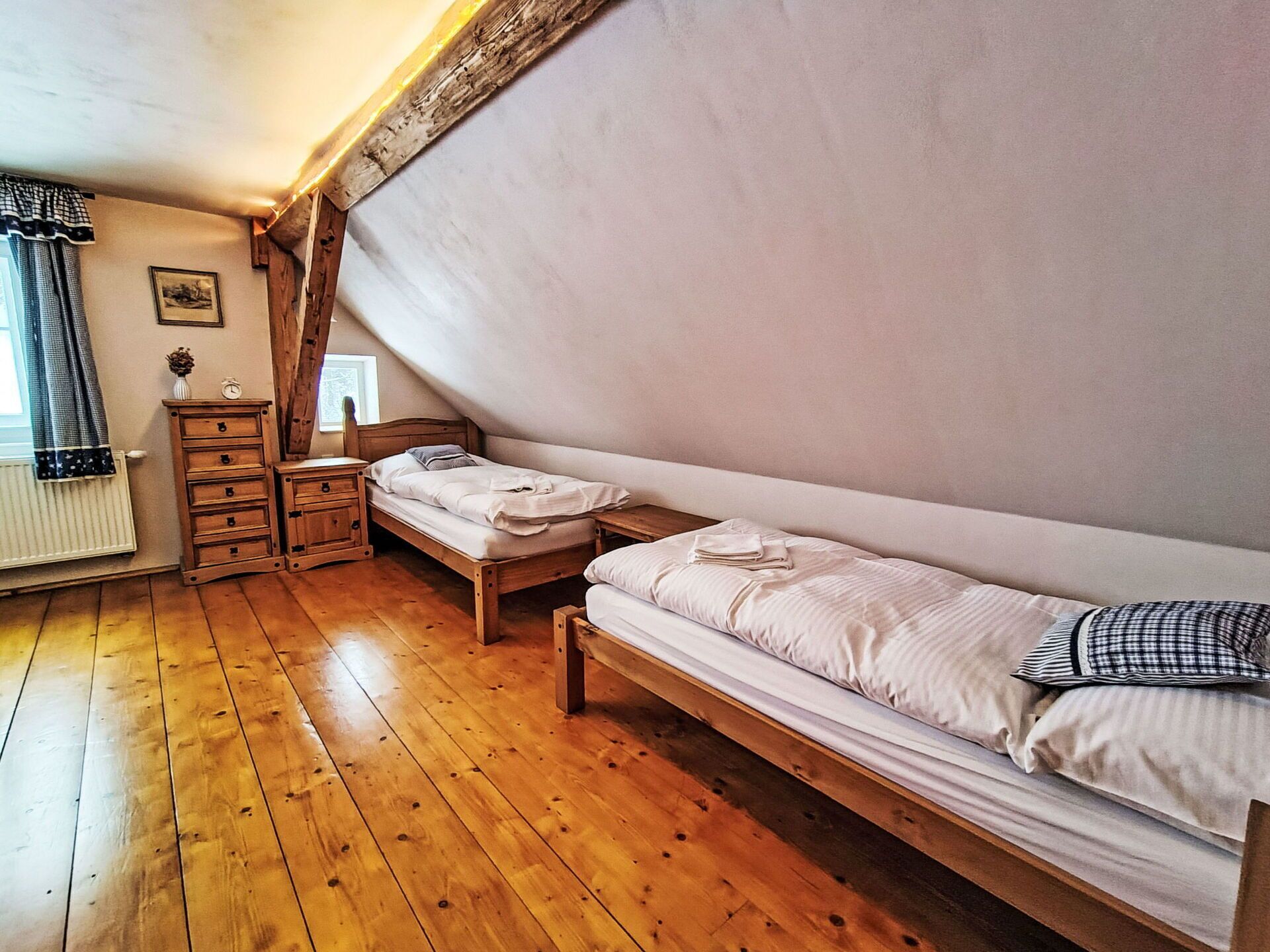 A room with wooden floors, two single beds, a wooden dresser, and a radiator.