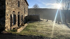 A stone building with a grassy yard, a small shed, and a clear sky.