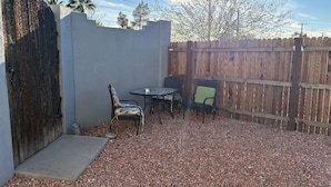 Un patio con mesa y sillas, cerca de madera y suelo de grava.