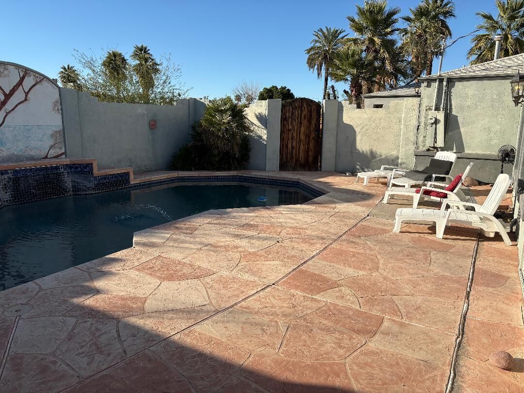 A swimming pool with a tiled deck, lounge chairs, and a palm tree backdrop.