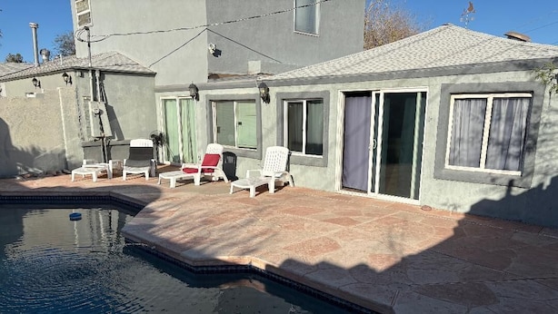 Una piscina con un borde de piedra, rodeada por una casa de fachada gris y tejado de baldosas.