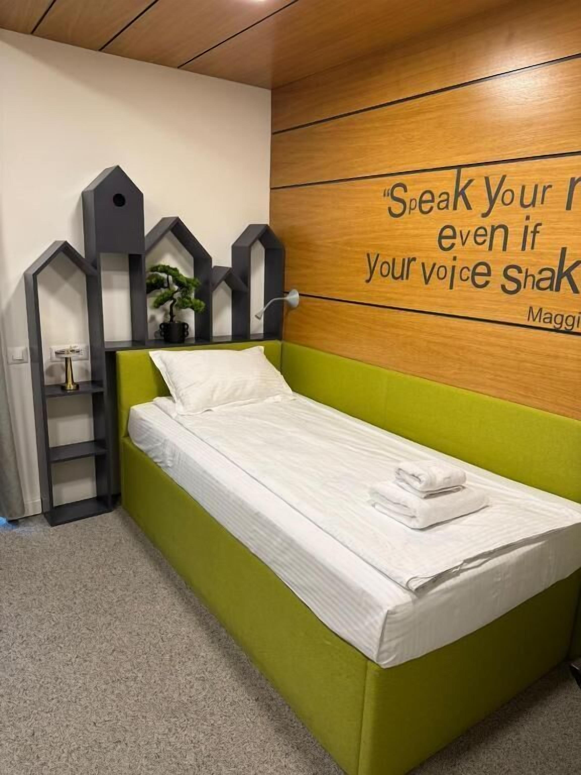 A single bed with a green headboard in a room with a wooden wall and a motivational quote.