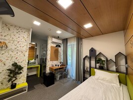 Habitación de hotel con cama, escritorio, silla, planta en maceta, espejo y ventana con cortinas.