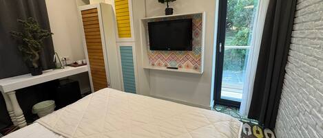 A bedroom with a bed, a TV mounted on the wall, a window with curtains, and a small potted plant on the dresser.
