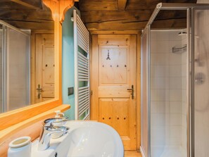 Une salle de bain avec une porte en bois, une douche et un lavabo avec un miroir.