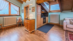 Ein gemütliches Zimmer mit Holzbalken, einer Küche, einem Heizkörper und einem fenster mit Vorhängen.