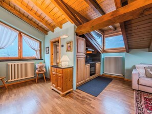 Ein gemütliches Zimmer mit Holzbalken, einer Küche, einem Heizkörper und einem fenster mit Vorhängen.