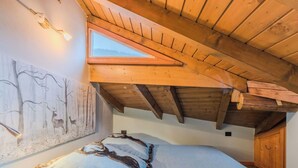 Ein Schlafzimmer mit schrägen Wänden, einem Oberlicht, einem Bett mit fellbesetztem Kopfkissen und einem Wandbild von Hirschen.