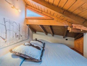 Ein Schlafzimmer mit schrägen Wänden, einem Oberlicht, einem Bett mit fellbesetztem Kopfkissen und einem Wandbild von Hirschen.