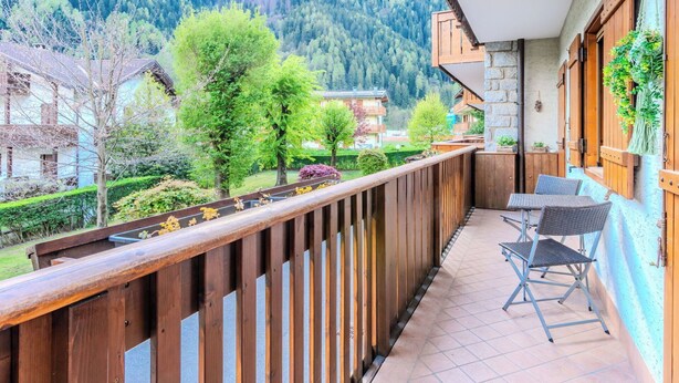 Een balkon met uitzicht op een bebost gebergte, een tafel met stoelen en een hangplant.