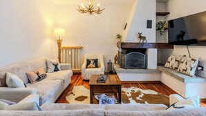 Een knusse woonkamer met een open haard, een zithoek, een salontafel en een kroonluchter.
