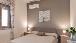A bedroom with a bed, nightstands, a wall-mounted air conditioner, a large floral artwork, and a window with curtains. - Wonderful private villa for 6 guests with A/C, WIFI, private pool, TV and patio (Syracuse)