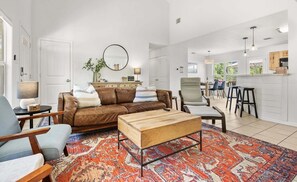 A modern living room with a brown leather sofa, a wooden coffee table, and a patterned rug. - Canyon Cottage: Hill Country Getaway, Hot Tub & Fire Pit, Mins to Whitewater Amphitheater & Tubing (Canyon Lake)